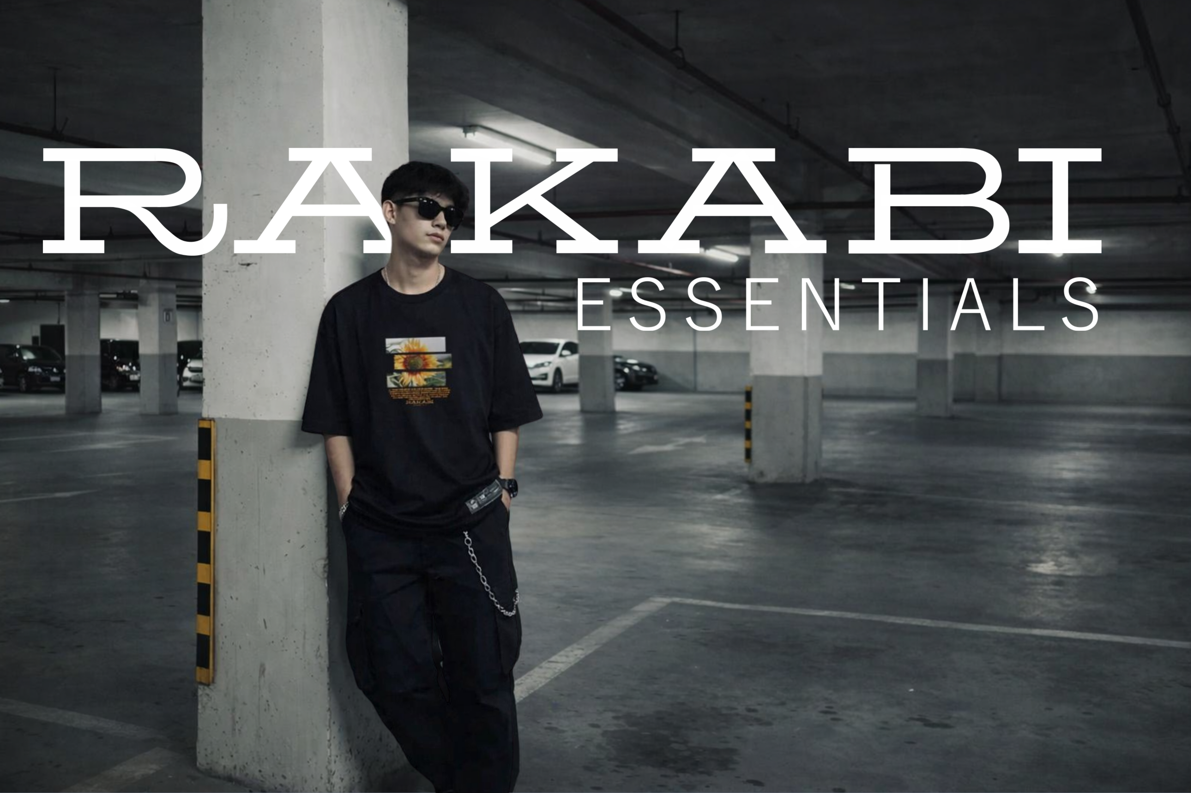 Person leaning against a pillar in an underground parking lot with 'RAKABI ESSENTIALS' branding.
